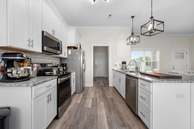 a kitchen with stainless steel appliances granite countertop a refrigerator a sink dishwasher a oven and a dining table with wooden floor