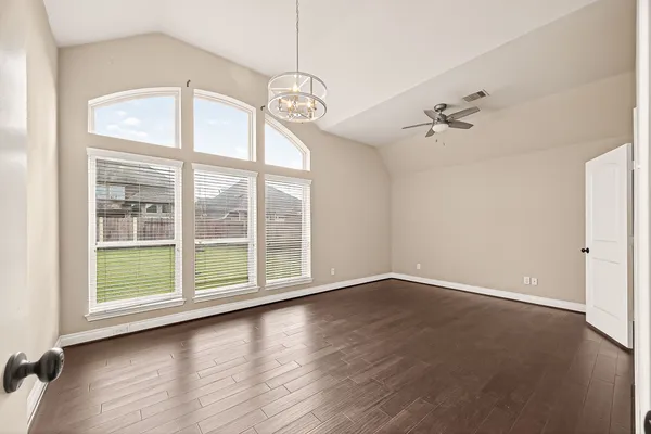 an empty room with wooden floor fan and windows