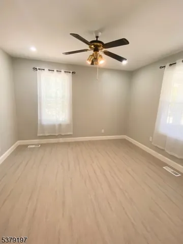 an empty room with wooden floor fan and windows