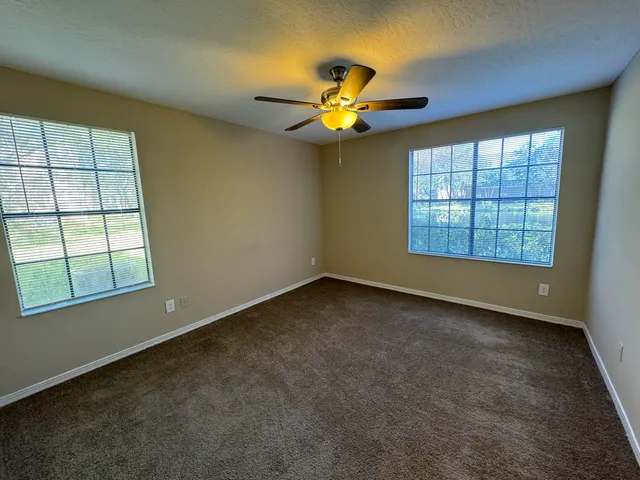 an empty room with windows and chandelier fan