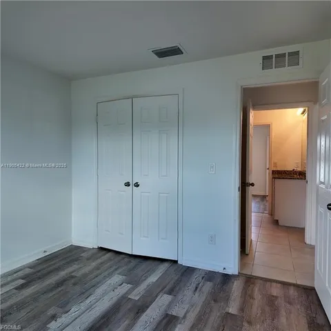 a view of an empty room with wooden floor and a bedroom