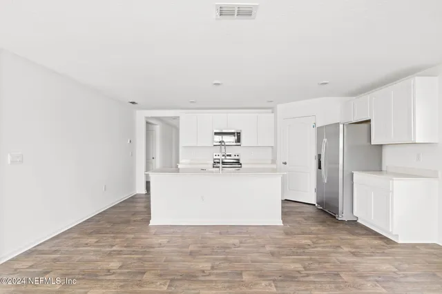 a view of kitchen with refrigerator stove and white cabinets with wooden floor