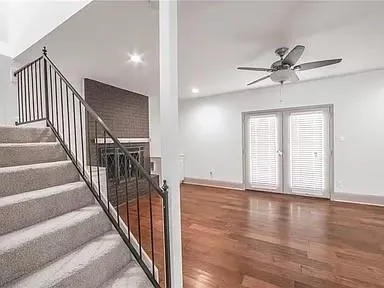 a view of an empty room with wooden floor and fan