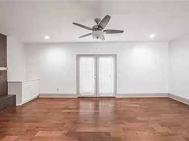 an empty room with wooden floor a ceiling fan and windows