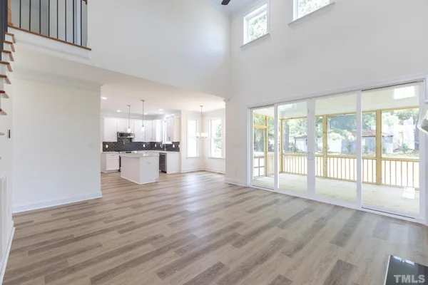 a view of an empty room with wooden floor and a kitchen