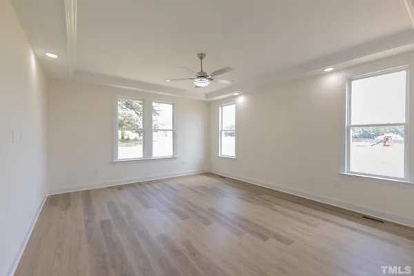an empty room with wooden floor chandelier fan and windows
