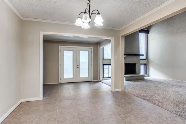 an empty room with a chandelier fan and kitchen view