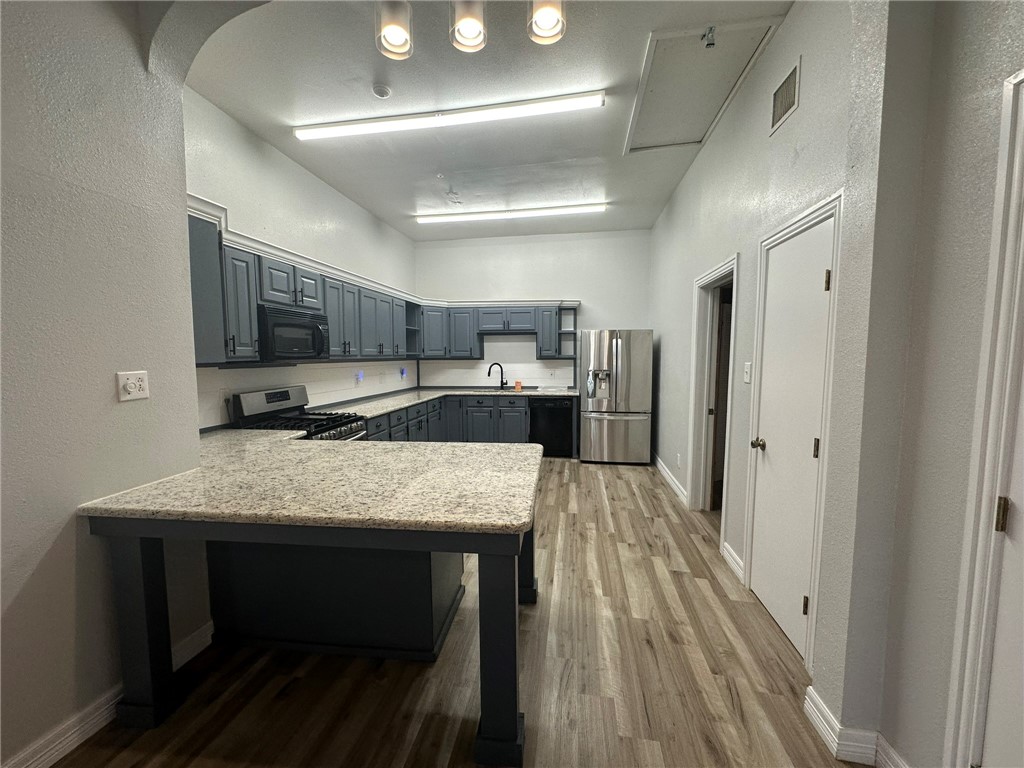 221 Commerce Street, Unit E Portland, TX 78374 - Photo 9 of 26 a large kitchen with stainless steel appliances kitchen island granite countertop a refrigerator oven a stove and a sink with wooden floor