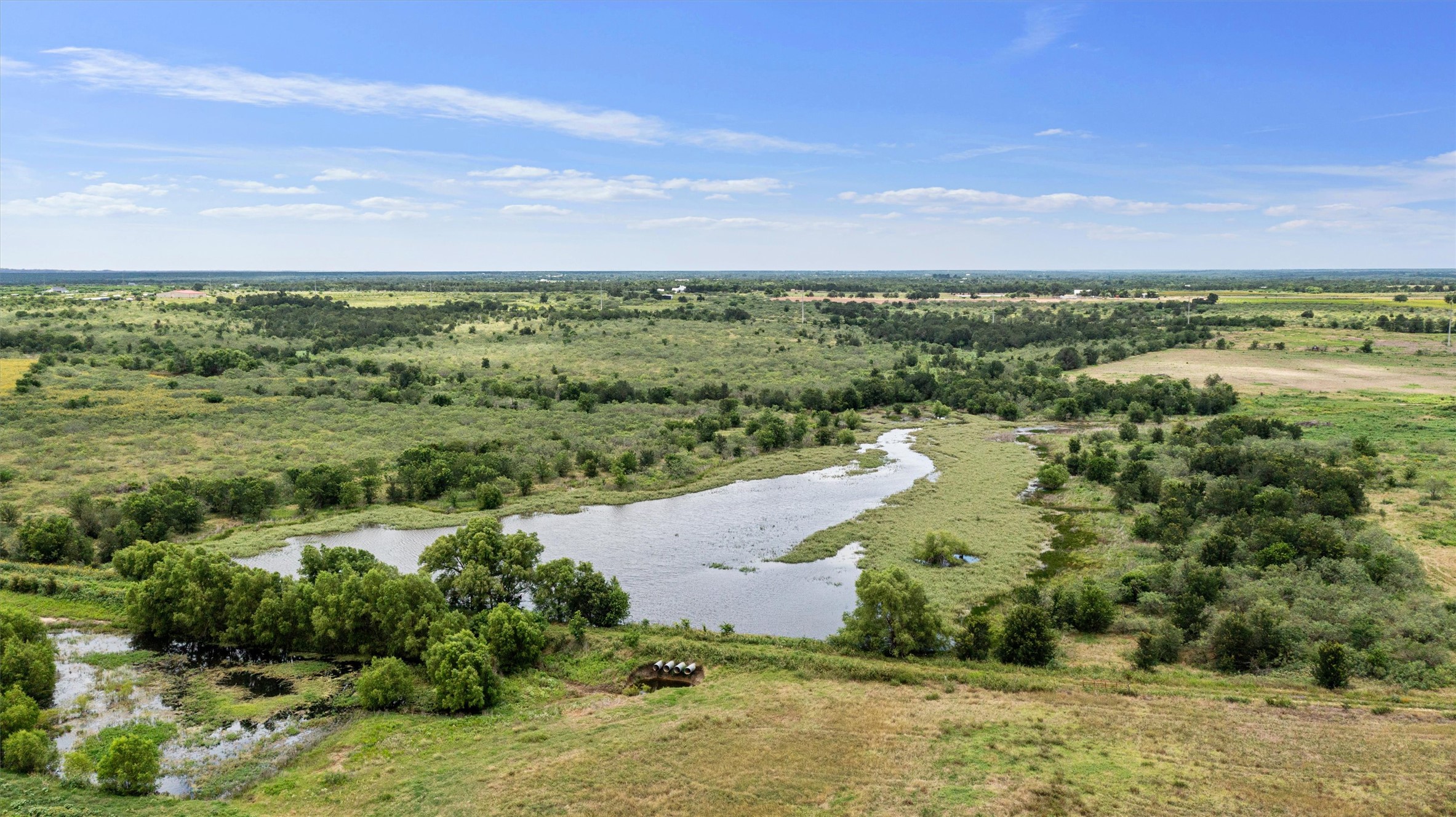 3315 County Road 463 Elgin, TX 78621 - Photo 5 of 32 Vast natural landscapes encompass a winding creek and verdant vegetation under an open sky.