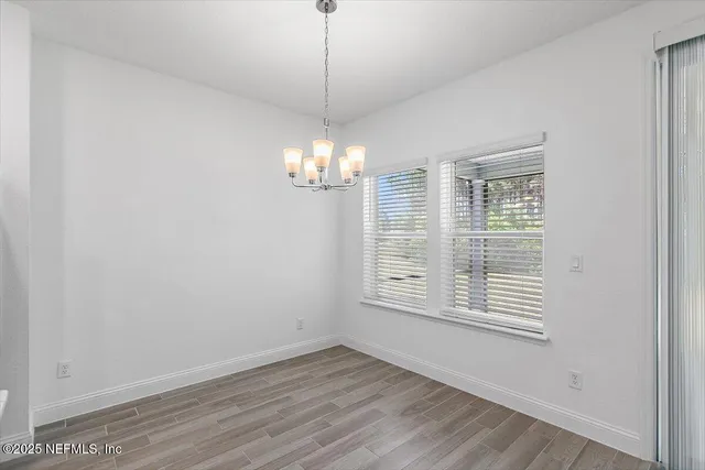an empty room with wooden floor chandelier and windows