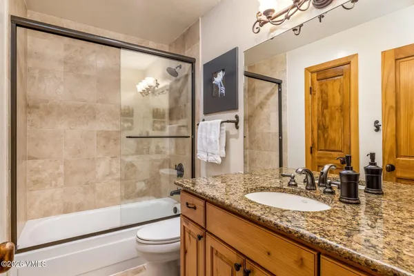 a bathroom with a granite countertop sink a toilet a mirror a vanity and shower