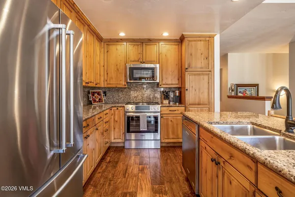 a kitchen with stainless steel appliances granite countertop a refrigerator a sink dishwasher a stove and a microwave oven with wooden floor