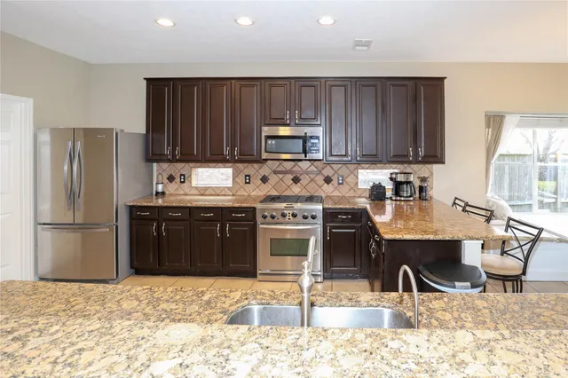 a kitchen with stainless steel appliances granite countertop a stove top oven a sink and a refrigerator
