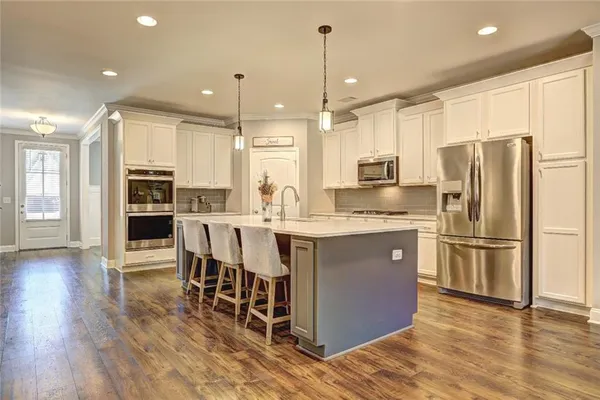 a kitchen with stainless steel appliances granite countertop a refrigerator a stove a sink a dining table and chairs with wooden floor