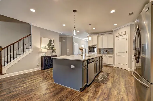 a kitchen with stainless steel appliances granite countertop a refrigerator a sink dishwasher a oven and a dining table with wooden floor