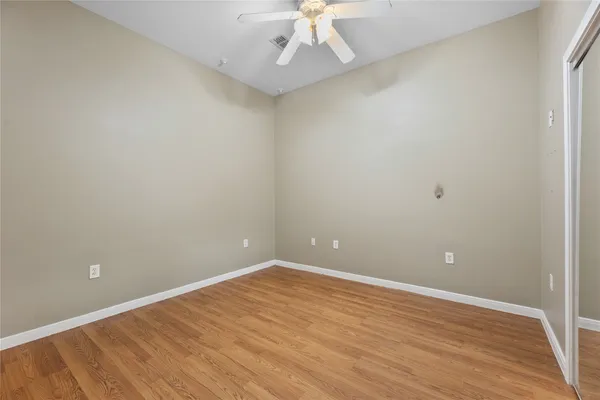 a view of an empty room with wooden floor and a ceiling fan