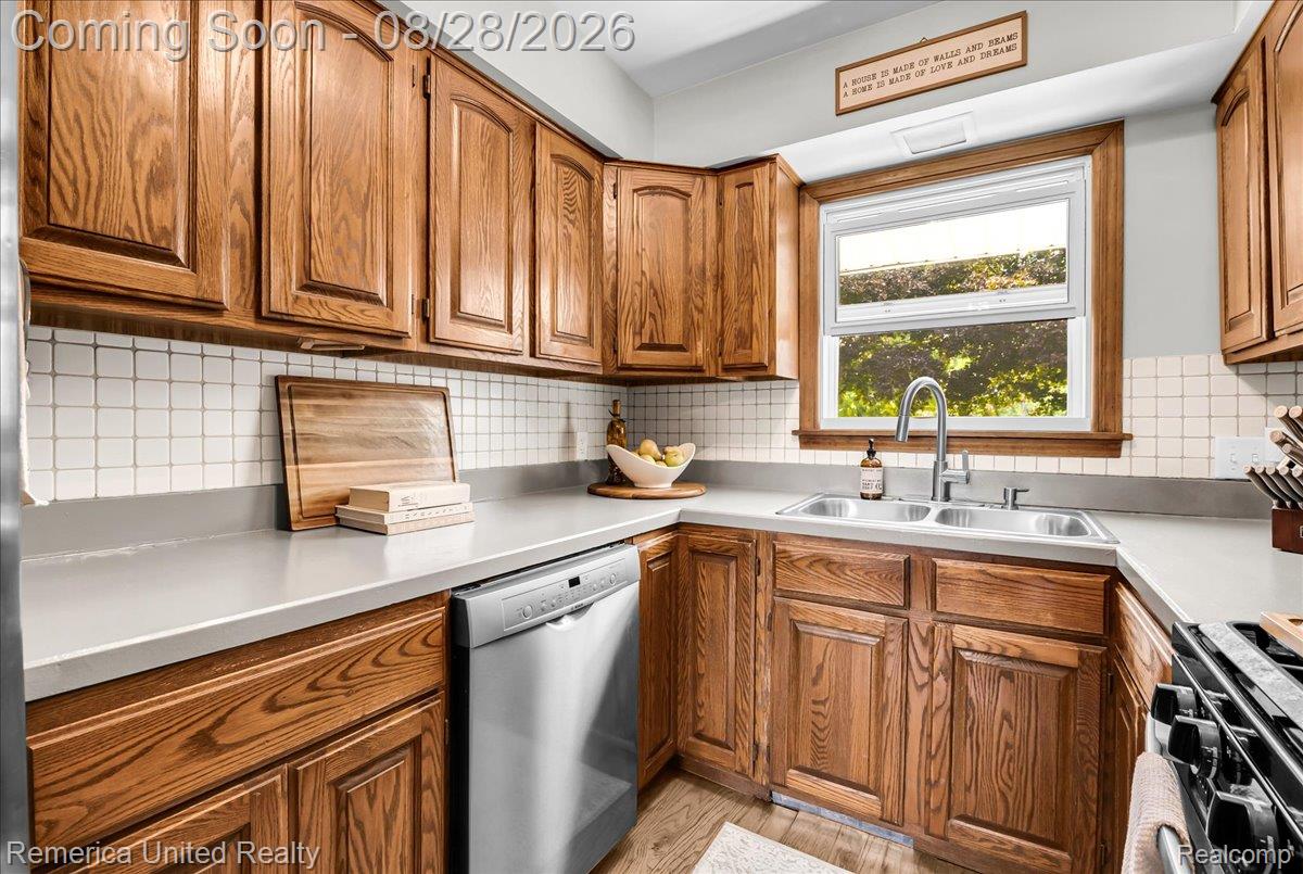 3687 Van Amberg Road Brighton, MI 48114 - Photo 11 of 56 Wood-finish cabinetry paired with solid surface countertops, square tile backsplash, and a stainless steel double basin sink with a gooseneck faucet