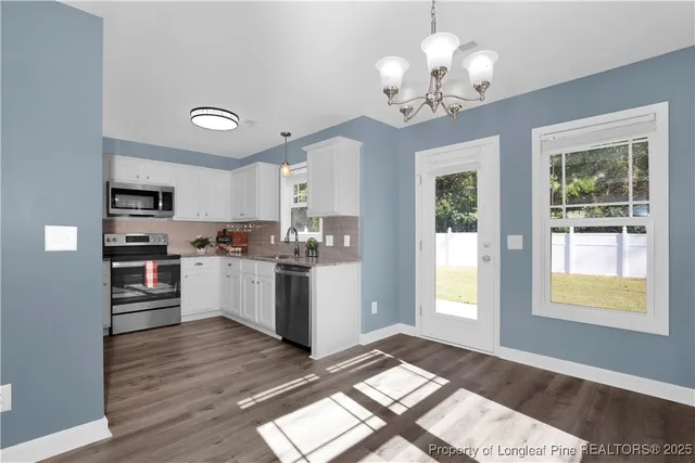 a kitchen with stainless steel appliances granite countertop white cabinets a refrigerator a sink a stove a dining table and chairs with wooden floor