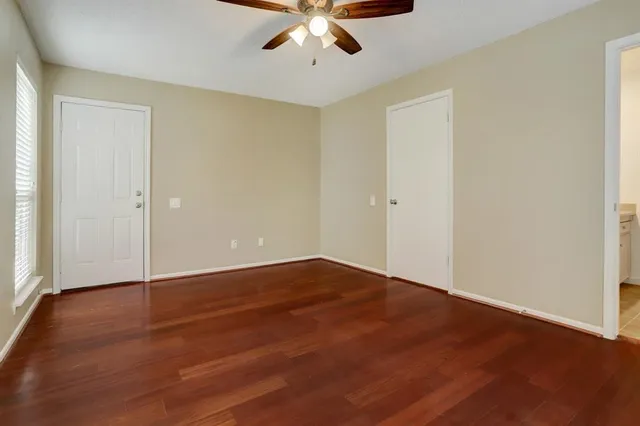 an empty room with wooden floor chandelier fan and windows