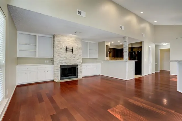 an empty room with wooden floor fireplace and windows