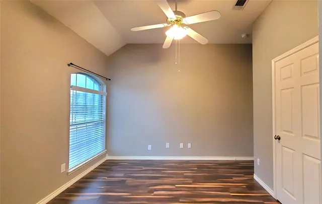 an empty room with wooden floor fan and windows