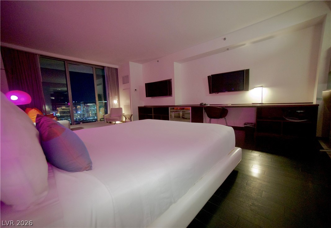 4381 West Flamingo Road, Unit 3616 Las Vegas, NV 89103 - Photo 8 of 29 City lights twinkle beyond the expansive windows of this chic bedroom, showcasing dark wood flooring.