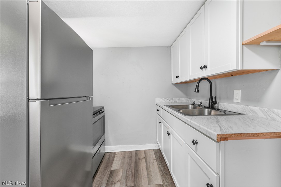 885 Wales Road Northeast Massillon, OH 44646 - Photo 4 of 34 Galley kitchen featuring stainless steel appliances, wood-finish flooring, white cabinetry with black hardware, a double basin sink with a matte black faucet, and light-toned countertops