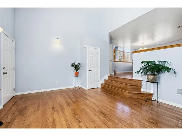 a view of an empty room and kitchen with wooden floor