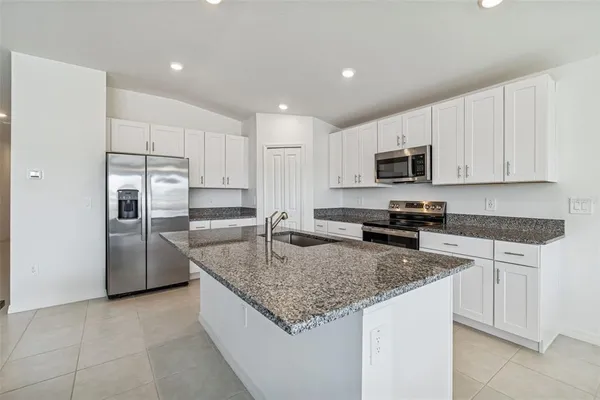 a kitchen with granite countertop a refrigerator a sink a stove a microwave and island