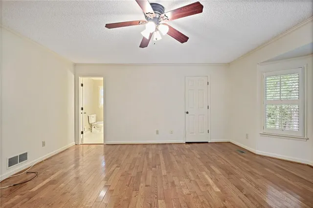 an empty room with wooden floor chandelier fan and windows