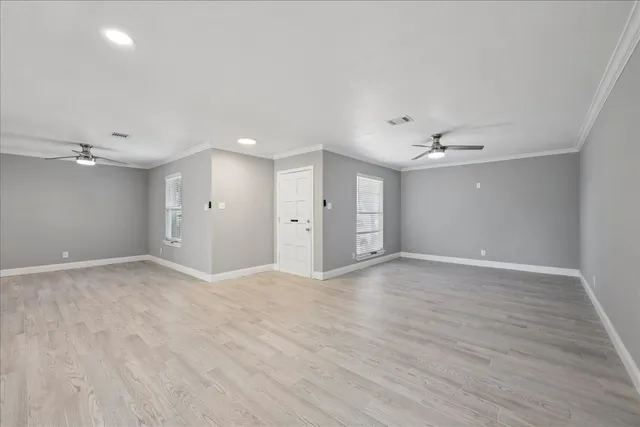 a view of an empty room with wooden floor and a ceiling fan