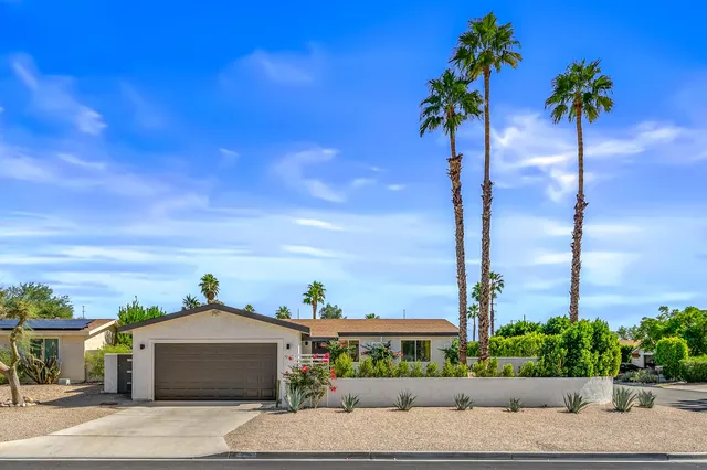 a front view of a house with a yard and palm trees