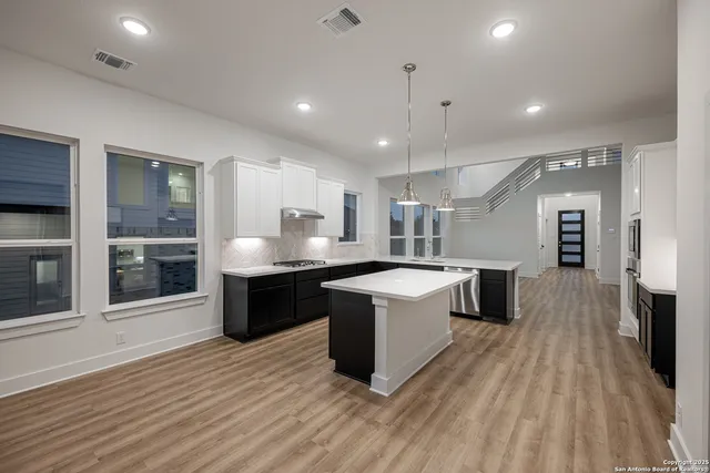 a large kitchen with a large counter top a sink stainless steel appliances and cabinets