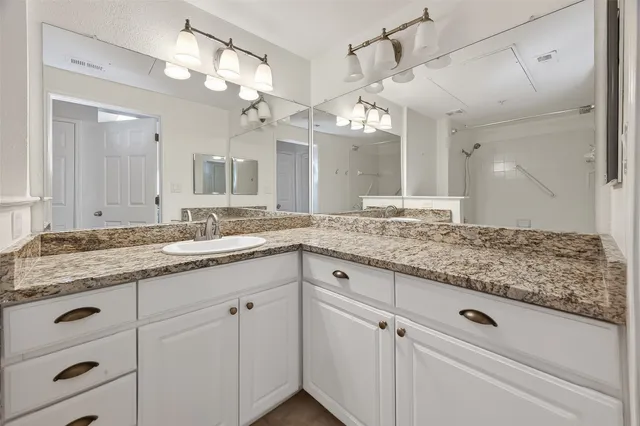 a bathroom with a granite countertop double vanity sink and mirror