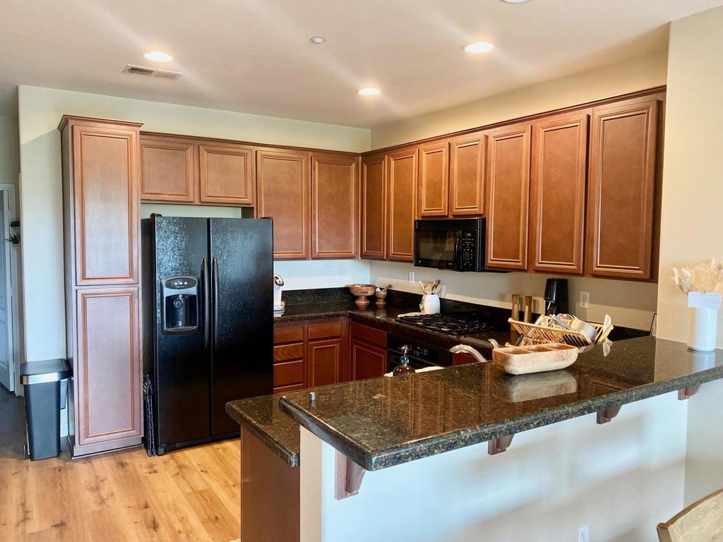 69 Via Sovana Santee, CA 92071 - Photo 3 of 17 a kitchen with granite countertop wooden cabinets a refrigerator and a sink