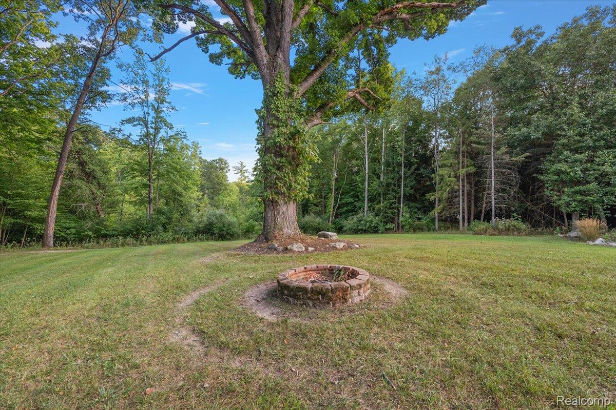 707 West Sutton Road Metamora, MI 48455 - Photo 8 of 84 Expansive lawn featuring a mature tree, brick-built fire pit, and a wooded perimeter