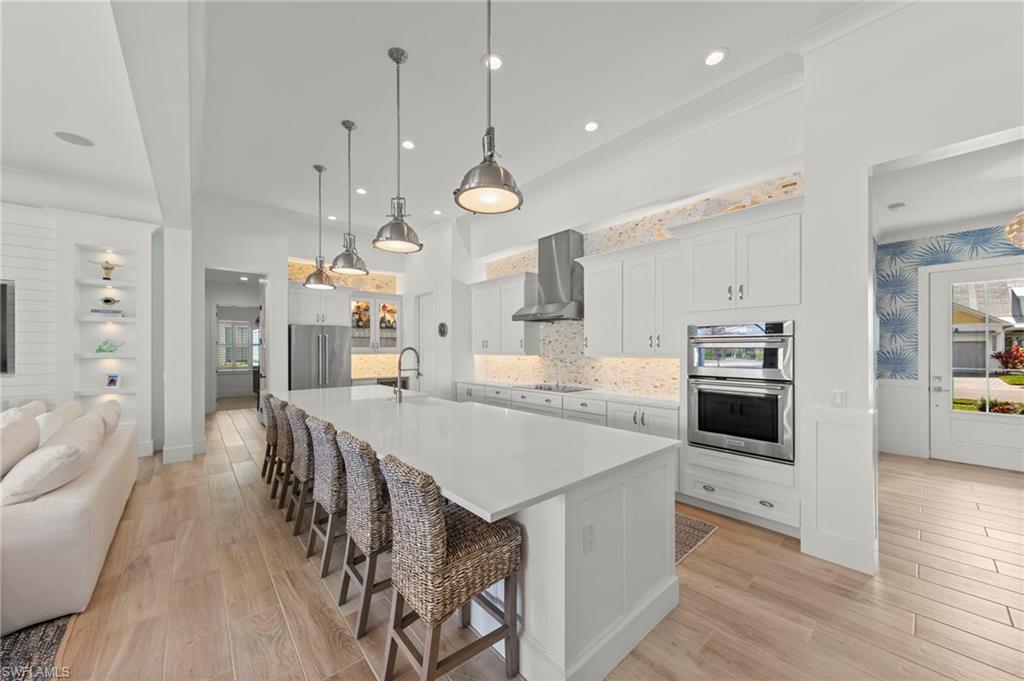 14785 Dockside Lane Naples, FL 34114 - Photo 10 of 50 Kitchen featuring a breakfast bar area, white cabinetry, light wood-style floors, a large island, and decorative light fixtures New KITCHEN PENDANTS (November 2018), New KITCHEN INTERIOR PAINT (July 2023)