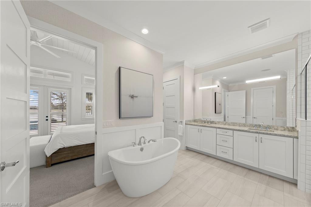 14785 Dockside Lane Naples, FL 34114 - Photo 15 of 50 Ensuite bathroom featuring double vanity, a soaking tub, wainscoting, and crown molding New CUSTOM MIRROR & SCONCES (February 2020), New WALLPAPER (June 2020), New PRIMARY BATH CEILING PAINT (July 2023)