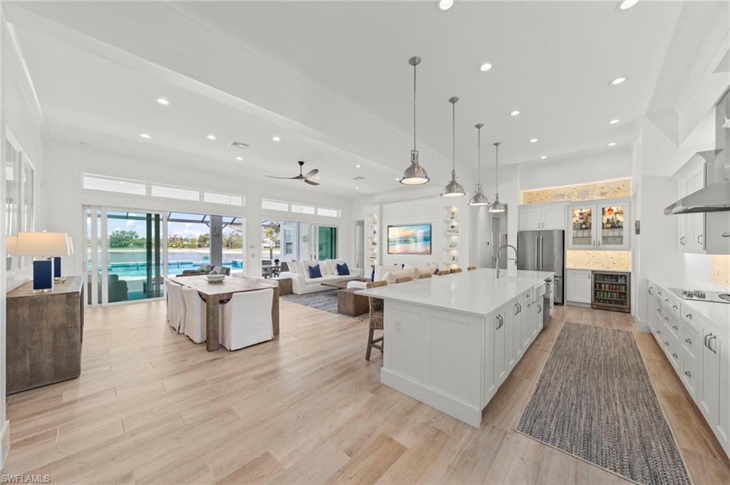 14785 Dockside Lane Naples, FL 34114 - Photo 50 of 50 Kitchen featuring open floor plan, a kitchen island with sink, decorative light fixtures, white cabinets, and a kitchen breakfast bar New MOUNTED TV & SONOS SOUND BAR (November 2018), New KITCHEN PENDANTS (November 2018), New SHIPLAP BUILT-IN & WALLS (May 2020), New KITCHEN INTERIOR PAINT (July 2023), new CEILING FAN (October 2024)