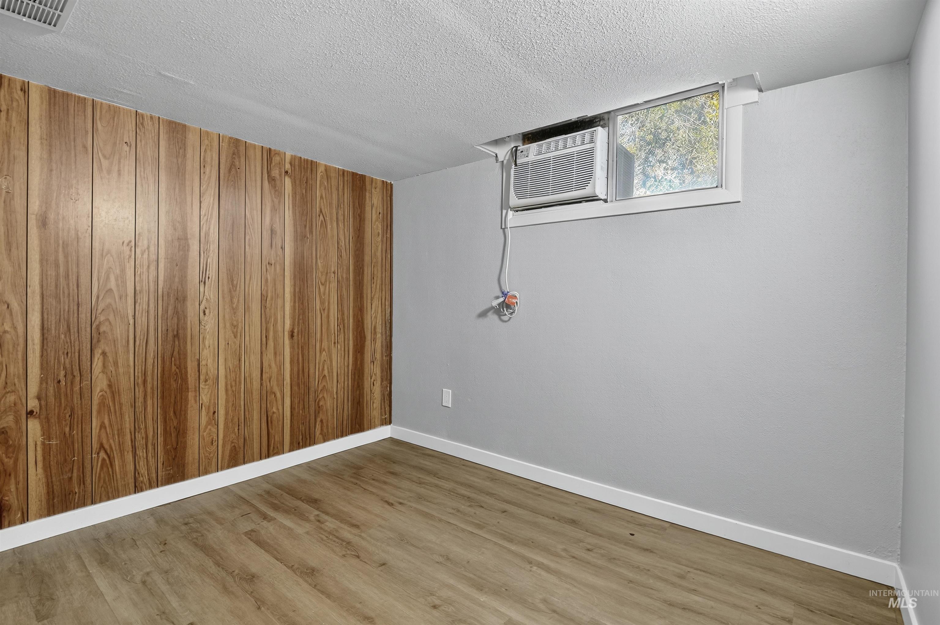 2118 West Targee Street Boise, ID 83705 - Photo 11 of 25 Empty room with wood finished floors, wooden walls, and a textured ceiling