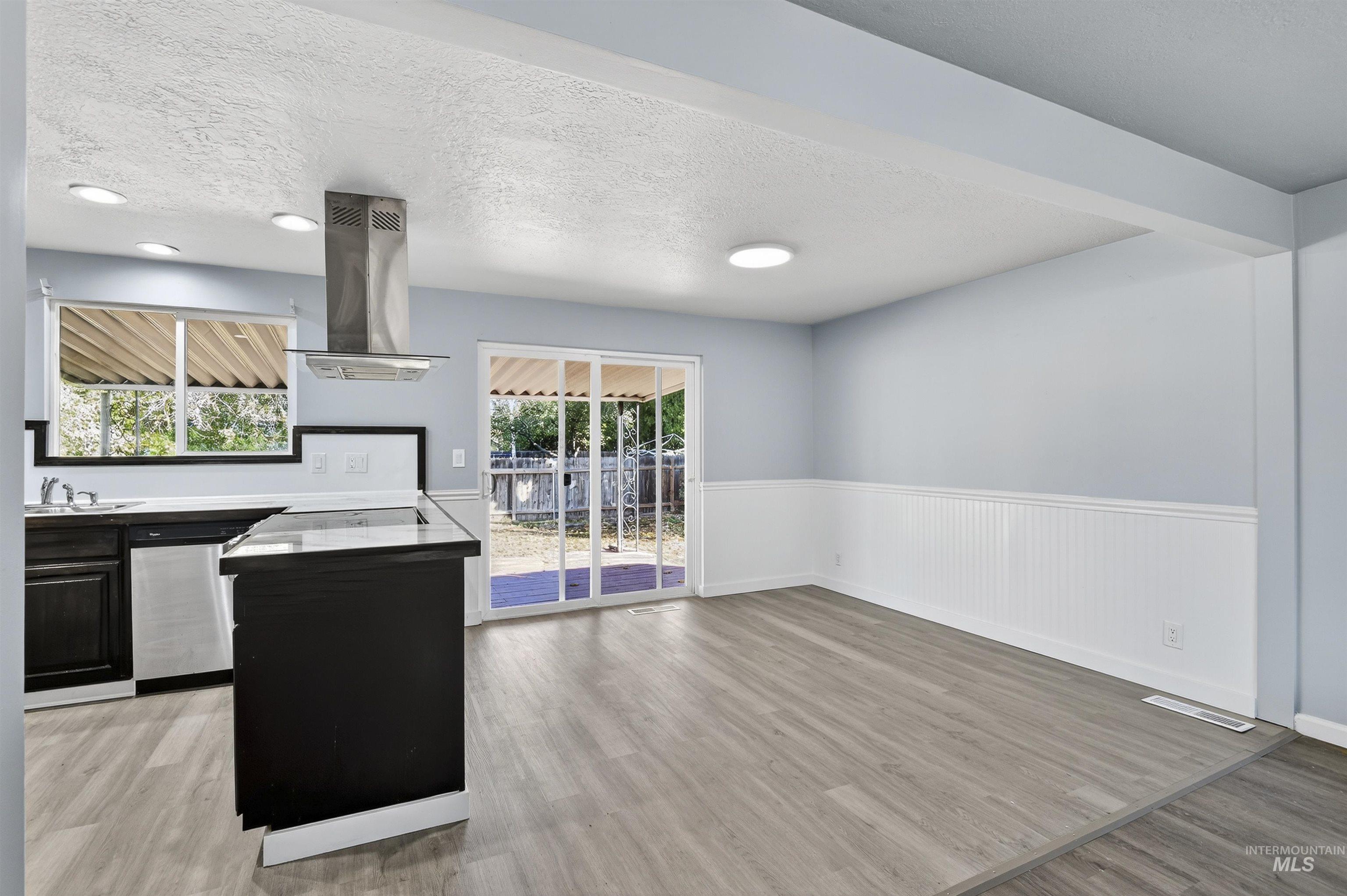 2118 West Targee Street Boise, ID 83705 - Photo 5 of 25 Kitchen with a textured ceiling, light wood-type flooring, island range hood, a wainscoted wall, and stainless steel dishwasher