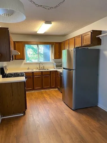 a kitchen with stainless steel appliances granite countertop a refrigerator a sink dishwasher a stove with wooden cabinets and wooden floor