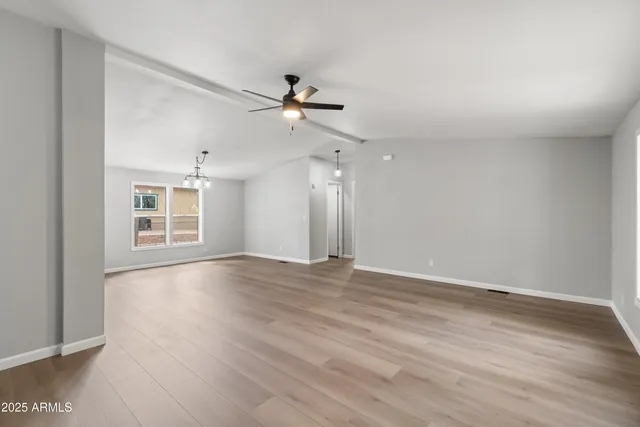 an empty room with wooden floor chandelier and windows