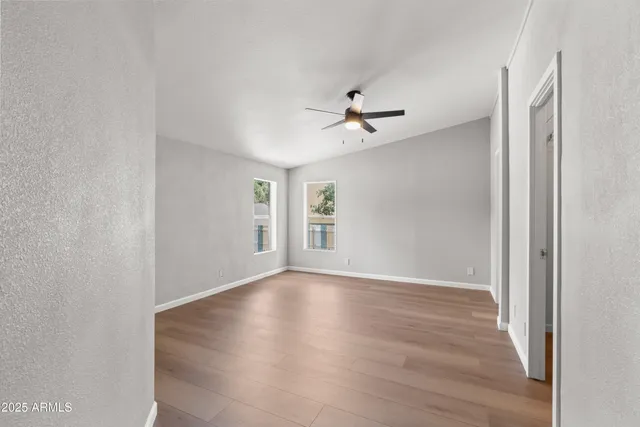 an empty room with wooden floor ceiling fan and windows
