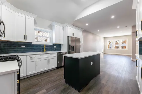 a kitchen with stainless steel appliances granite countertop wooden cabinets a sink a stove a refrigerator and wooden floors