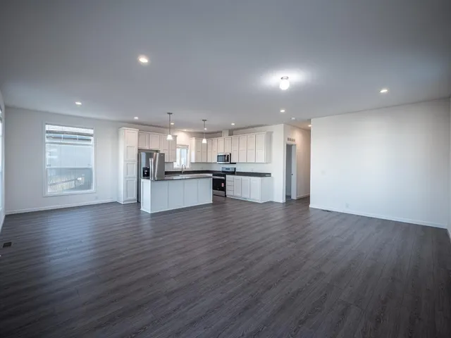 a kitchen with stainless steel appliances granite countertop a refrigerator a stove a microwave oven a sink and white cabinets with wooden floor