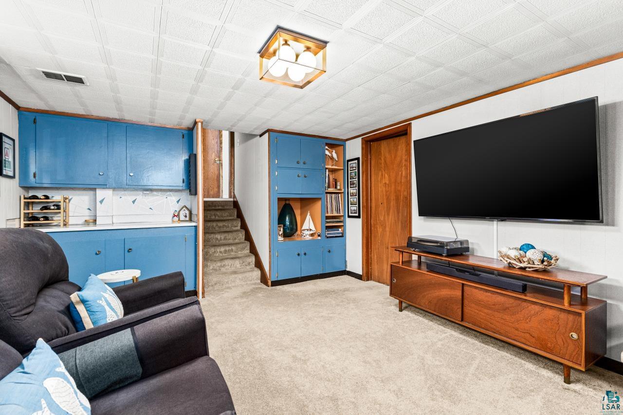 4119 Pitt Street Duluth, MN 55804 - Photo 38 of 50 Carpeted recreation room featuring extensive blue cabinetry, built-in shelving, white paneled walls, and a textured ceiling