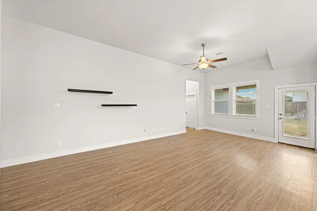 an empty room with wooden floor chandelier fan and windows