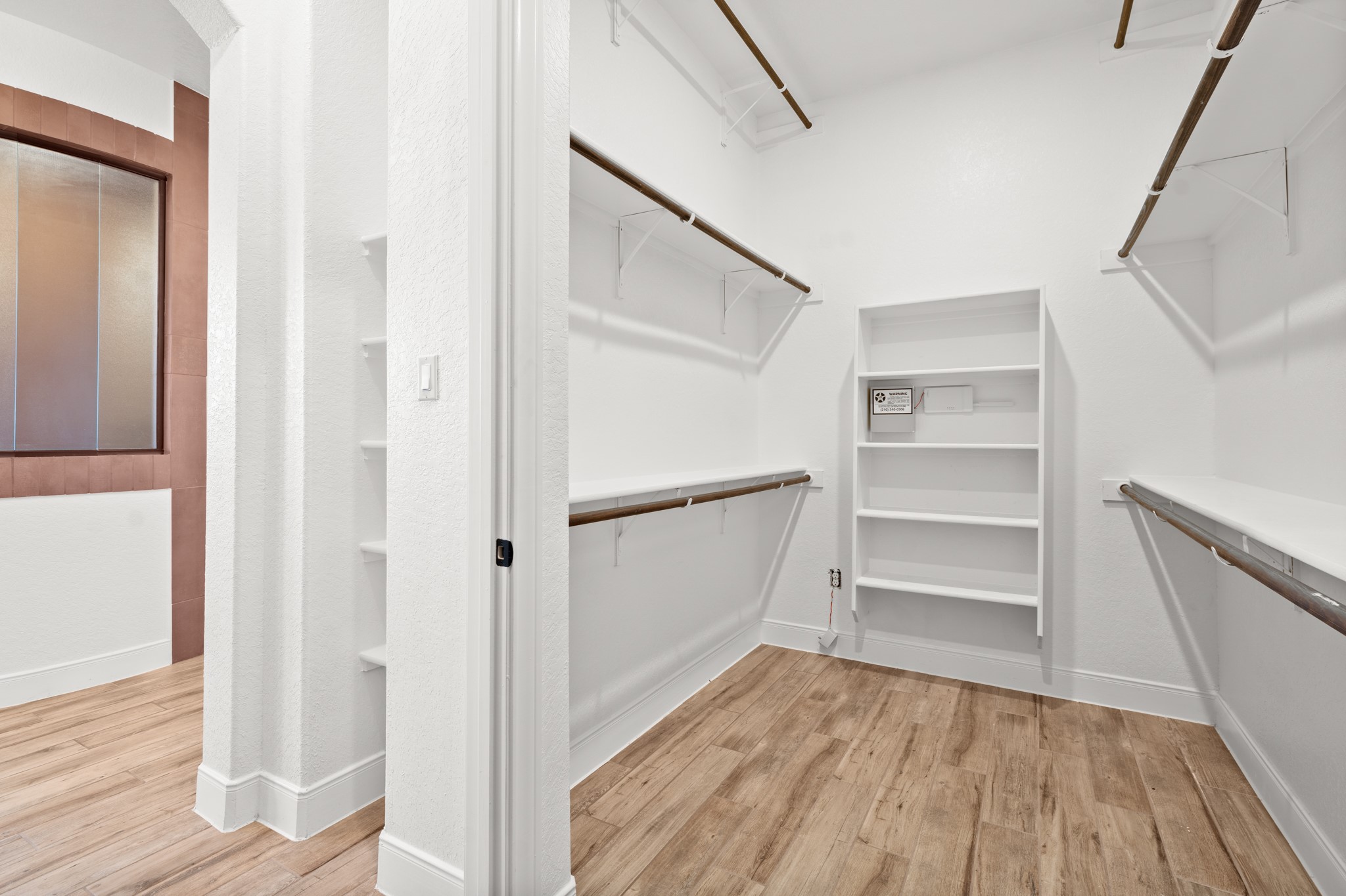 128 Hiram Cook Blanco, TX 78606 - Photo 20 of 40 Walk-in closet featuring wood-finish flooring, white walls, multiple hanging rods, built-in shelving, and a frosted window with wood trim