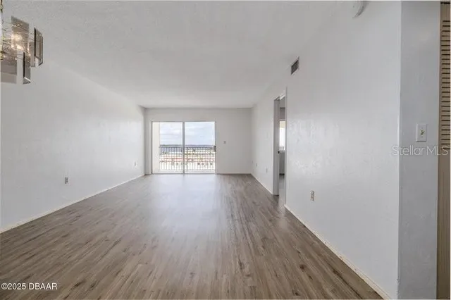 a view of an empty room with wooden floor and a window
